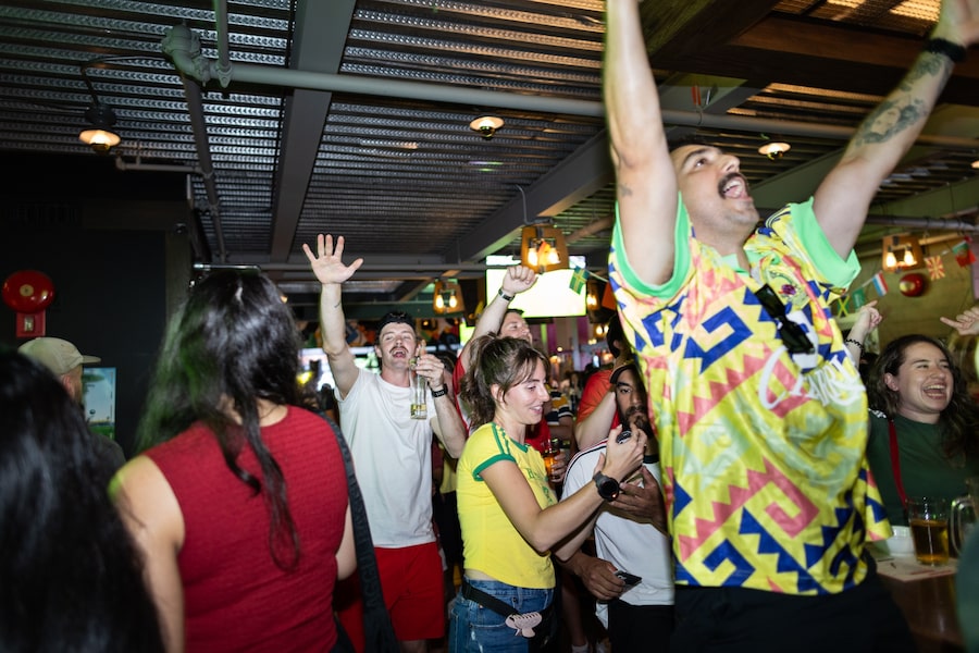 Server Kaylee Banks, centre, settles a customer’s tab at Good Co. sports bar on Granville Street in downtown Vancouver, as fans celebrate Mexico's goal against Czechia.