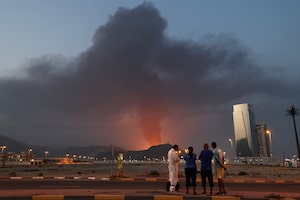 Foreign workers look at a tall plume of black smoke ascends following an explosion in the Fujairah industrial zone on March 3, 2026. Iran's strikes on Gulf neighbours since February 28, following the US-Israeli attack, forced the UAE to shut its airspace, blindsiding travellers who thought they were headed to one of the region's safest holiday destinations. (Photo by Fadel SENNA / AFP via Getty Images)
