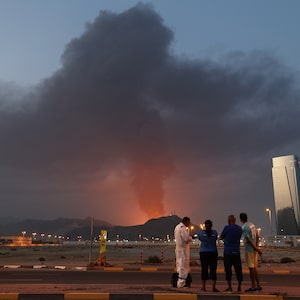 Foreign workers look at a tall plume of black smoke ascends following an explosion in the Fujairah industrial zone on March 3, 2026. Iran's strikes on Gulf neighbours since February 28, following the US-Israeli attack, forced the UAE to shut its airspace, blindsiding travellers who thought they were headed to one of the region's safest holiday destinations. (Photo by Fadel SENNA / AFP via Getty Images)