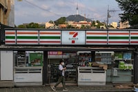A pedestrian walks past a 7-Eleven convenience store as the Seoul Tower is seen in the background in Seoul on July 6, 2026. (Photo by Jade GAO / AFP via Getty Images)