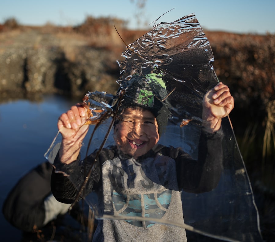 On a road warped by thawing permafrost and pocked with puddles, James Schaeffer, 7, breaks off ice to play with. It is late September here in Kotzebue, Alaska, in the warmest Arctic autumn on record.