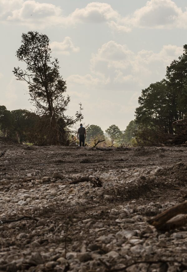 A man walks along the bank of the Guadalupe River in Kerville, Tex., after flood waters have receded.
