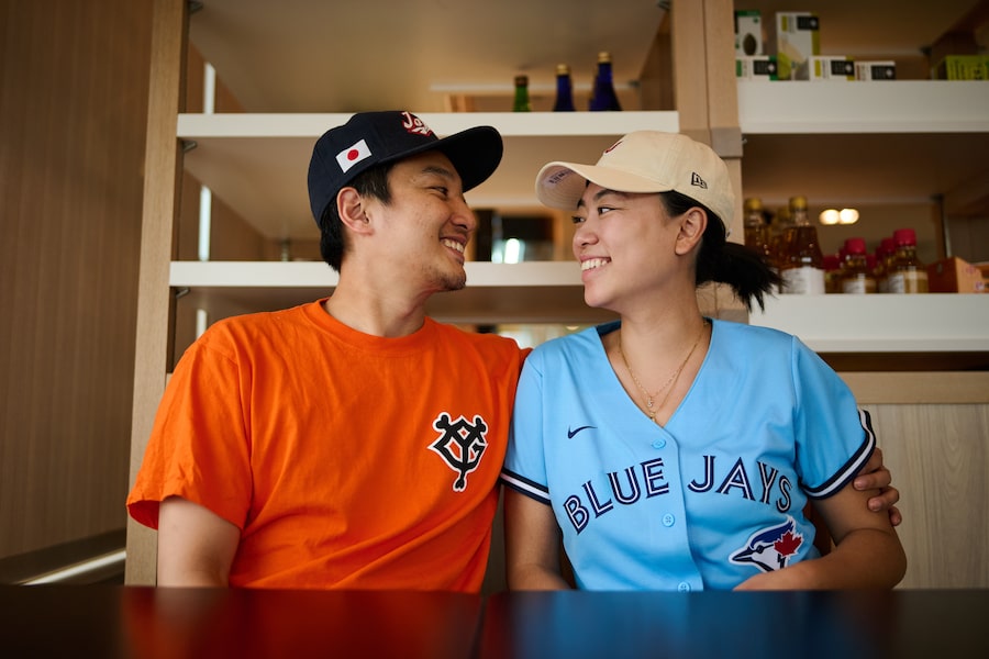 Sean Akiyama and Nicole Lin, dressed in baseball gear at his father’s seafood restaurant, say they’re looking forward to cheering on the Toronto Blue Jays as Kazuma Okamoto joins the roster.